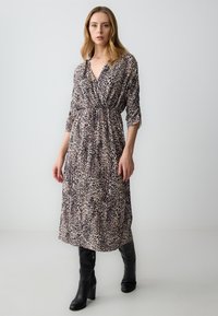 Leopardenmuster-Midi-Kleid mit V-Ausschnitt und geknotetem Taillenbereich, langen Ärmeln, fließendem Stoff, kombiniert mit knielangen schwarzen Stiefeln.