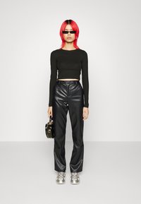 Črn rebrast crop top, črne usnjene hlače z visokim pasom, srebrni športni copati in majhna okrogla črna torbica. Model nosi majhne črne sončne očala.