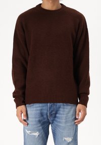 Hnědý pletený svetr s kulatým výstřihem a žebrovanými manžetami, nošený s modrými džíny s potrhanými detaily. Měkká textura, volný střih, minimalistický design.