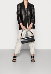 Blazer in pelle nera sopra una canotta a righe bianche e nere, pantaloni crema e sandali con plateau neri. Tiene una piccola borsa nera.