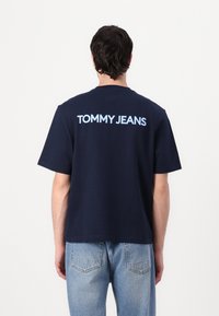 Navy blue cotton T-shirt with short sleeves, featuring light blue “TOMMY JEANS” text across the back. Casual fit and straight hem.