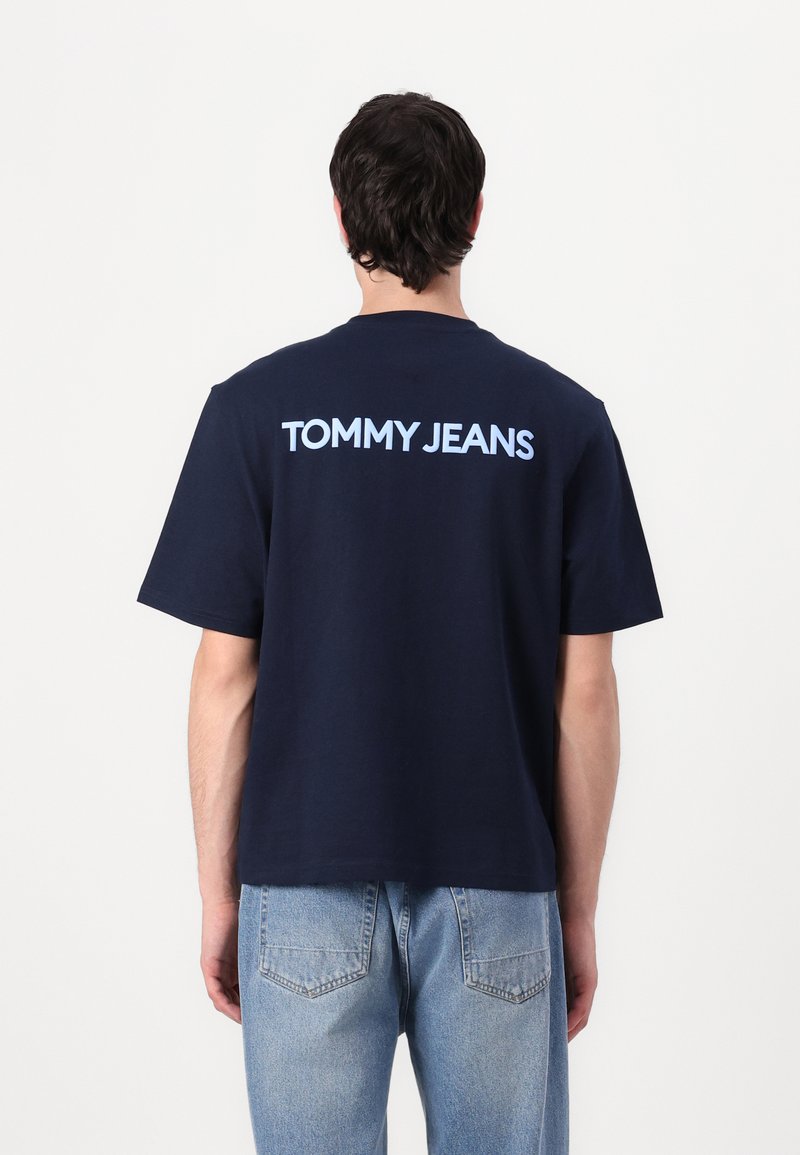 Navy blue cotton T-shirt with short sleeves, featuring light blue “TOMMY JEANS” text across the back. Casual fit and straight hem.