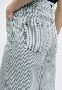 Jean en denim rayé à taille haute, présentant de fines rayures verticales bleues et blanches, des poches latérales et arrière, et une coupe légèrement décontractée.
