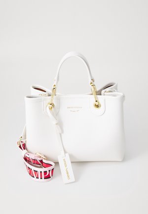 Sac à main en cuir blanc avec garnitures dorées, deux poignées et une bandoulière amovible rouge et rose avec inscriptions blanches. Nom de la marque embossé sur le devant.