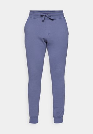 Lilla treningbukser laget av myk stoff, med elastisk midjebånd, snøring detaljer, og avsmalnende bein med ribbede mansjetter.