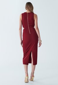 Rotes, figurbetontes Midikleid mit hohem Schlitz, ärmellosem Design und Reißverschluss, der sich am Rücken entlangzieht. Es zeichnet sich durch eine glatte Textur und eine maßgeschneiderte Passform aus.