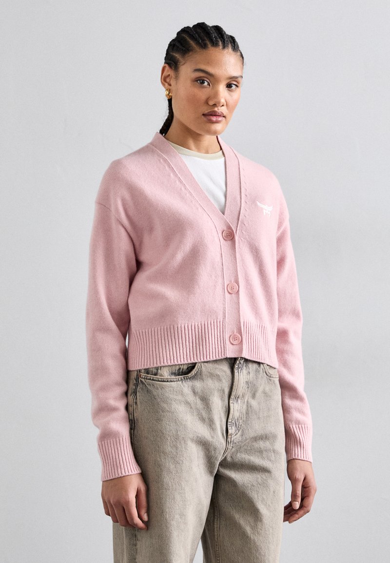 Lichtroze cropped cardigan met een V-hals, geribbelde onderrand en knopen. Heeft subtiele borduursels en een zachte textuur, gecombineerd met hoog aansluitende beige broek.