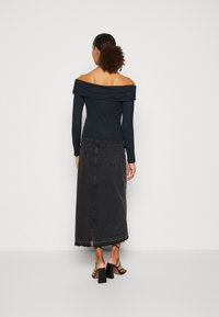 Svart off-shoulder-topp med långa ärmar, kombinerad med en svart denim maxikjol med fransad fåll och en slits i ryggen.
