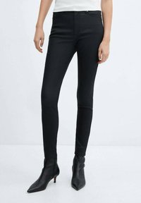 Černé slim-fit džíny s hladkou, elastickou texturou, s mírně zvýšeným pasem a klasickým pětivreckovým střihem, doplněné o špičaté černé podpatky.