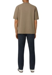 Brązowy T-shirt z krótkim rękawem i okrągłym dekoltem, zestawiony z ciemnoniebieskimi dżinsami. Model stoi tyłem, ukazując minimalne szwy i teksturę.