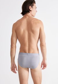Slip grigio realizzato in tessuto morbido, con una superficie liscia e cintura elastica. L'immagine mostra il retro di un modello maschile.