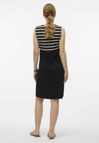Black sleeveless dress with a striped panel at the top. Smooth fabric, knee-length cut, and simple design. Worn with flat sandals.