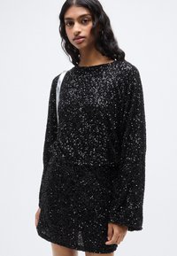 Μαύρο φόρεμα με παγιέτες, μακριά μανίκια, στρογγυλή λαιμόκοψη και ελαφρώς άνετη εφαρμογή. Η υφή διαθέτει λαμπερές παγιέτες που προσδίδουν λαμπερό εφέ.