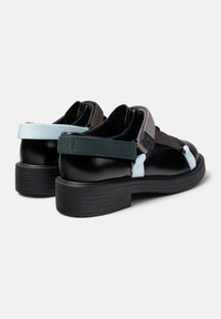 Zapatos de cuero negro con un tacón grueso. Cuentan con correas ajustables en gris y verde oscuro, con acentos en azul claro a los lados.