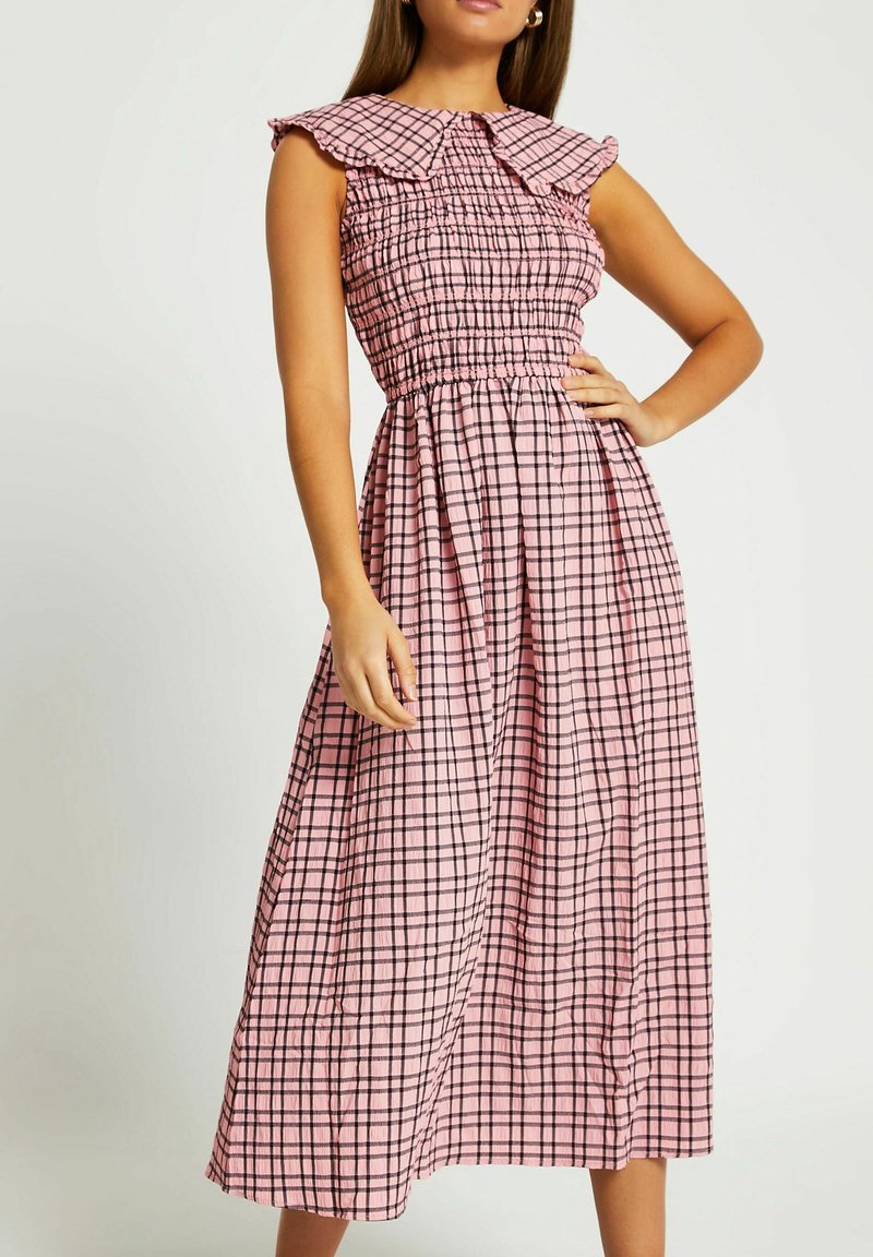 Rosa routad midi-klänning med smockad liv, volangkrage och ärmar i armbågs längd. Har en lätt kjol och rutmönster med svarta accenter.