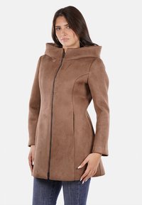Cappotto in suede marrone con un grande cappuccio, zip frontale e silhouette aderente. La texture è liscia e le maniche sono leggermente svasate.