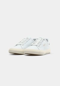 White low-top sneakers with smooth leather upper, round toe, and rubber sole. Features flat laces and subtle branding on the side.