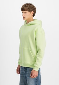 Felpa verde chiaro realizzata in tessuto morbido, con tasca a marsupio e cappuccio regolabile. Abbinata a jeans blu.