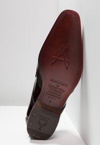 Semelle de chaussure en cuir présentant une couleur bordeaux profond, une surface texturée et un marquage gravé. Le design notable comprend un bout pointu et des détails faits à la main.