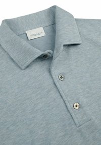 Helles blaues Poloshirt aus weichem, strukturierter Stoff. Mit einem Kragen-Ausschnitt, zwei Knöpfen und einem Etikett mit der Aufschrift "Profuomo".