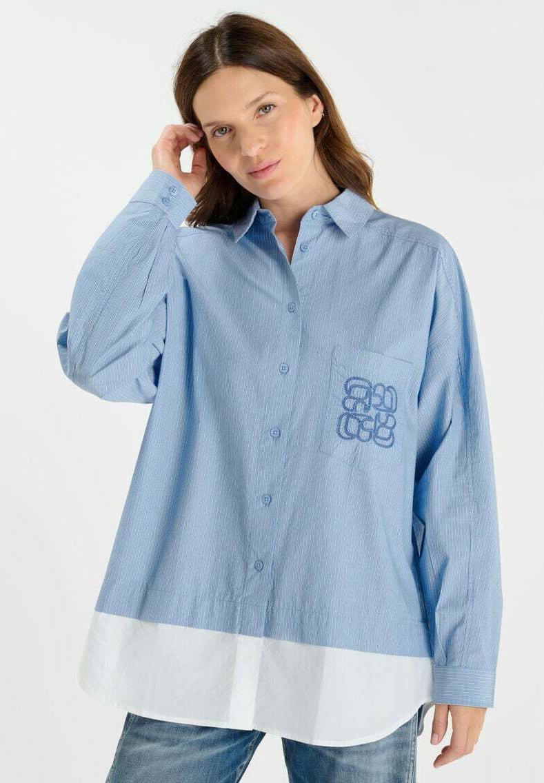Lichtblauw gestreept oversized shirt met een witte zoom. Heeft een knoopsluiting aan de voorkant en een zak met een blauw grafisch ontwerp.