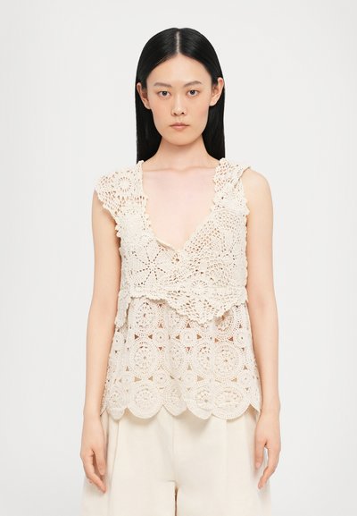 Crochet top in cream color featuring a deep V-neck, scalloped edges, and intricate floral patterns. Lightweight, layered design.