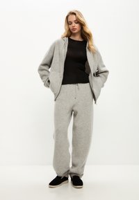 Grijze hoodie en joggingsbroek set gemaakt van zachte stof, met een relaxte pasvorm en een trekkoord in de taille. Zwarte top eronder, met zwarte instappers.