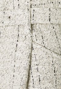 Tela blanca tejida con una apariencia texturada, con hilos negros sutiles y acentos metálicos, que muestra un diseño estructurado.