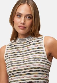 Stricktops ohne Ärmel mit einem hohen Kragen, mehrfarbigen horizontalen Streifen in Gelb, Blau, Rot und Schwarz auf einem cremefarbenen Hintergrund.