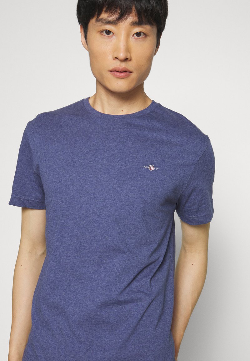 Männer T-Shirt mit kurzen Ärmeln aus dunkelblauer Baumwolle, rundem Halsausschnitt und kleinem gestickten Emblem auf der Brust. Glatte Oberfläche.