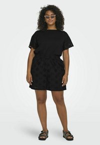 Crna pamučna majica s izrezanim, vezenim kratkim rukavima i odgovarajućim šortsevima sa cvjetnim izrezima. Nositi s modrim sandalama na remen.