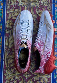 Scarpe da calcio rosse e bianche, con intricati motivi floreali e dettagli dorati, dotate di una parte superiore strutturata e tacchetti prominenti. Lacci bianchi.