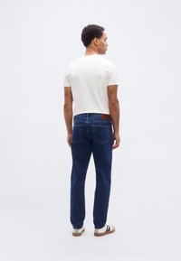 Σκούρα μπλε τζιν με ίσια γραμμή, λευκό μπλουζάκι και casual παπούτσια. Σημαντικά χαρακτηριστικά είναι ένα δερμάτινο πίσω ταμπελάκι και ελάχιστο ράψιμο.