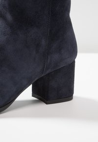Navy Wildleder-Stiefelette mit Blockabsatz, glatter Textur, klaren Linien und minimalen Nähten in der Nähe der Naht.