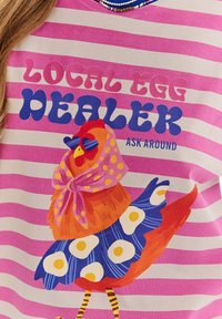 Tílko s krátkým rukávem, které má horizontální růžové a bílé pruhy, s barevným grafikou slepice v šále a vzorovaných šatech.