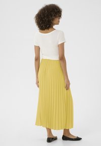 Top bianco a maniche corte abbinato a una lunga gonna gialla plissettata. Ballerine nere completano l'outfit. Tessuto morbido e design a strati.
