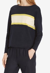 Felpa navy con scollatura rotonda, caratterizzata da righe orizzontali gialle e crema sul petto. Texture morbida, vestibilità rilassata.