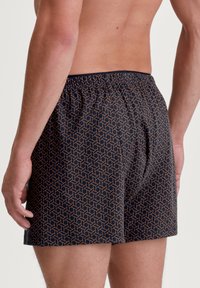 Heren boxershort van marineblauwe stof met een geometrisch patroon in goud. Bevat een elastische tailleband en heeft een ontspannen pasvorm met een detail van een middenventilatie.