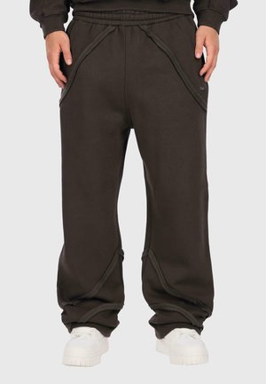 Dark brown sweatpants made of soft material, featuring curved side pockets, an elastic waist, and a relaxed fit, paired with white sneakers.