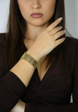 Gold-tone bangle bracelet with multiple stacked wire strands. Smooth texture and circular shape. Worn on a wrist against a dark top.