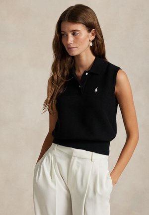 Must varrukateta polo ribikujulise tekstuuriga, millel on kolme nupuga plastron ja tikitud logo. Sobitatud koorevärviliste volditud pükstega.