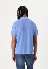 Kortermet polo skjorte i lyseblått, med teksturert stoff, klassisk krage, og rett kant. Brukt med blå jeans.