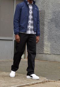 Granatowa kurtka na zamek na koszulę w kratę, czarne spodnie i białe trampki. Kurtka ma elastyczne mankiety i logo na piersi.