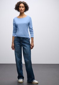 Lichtblauw langemouwen shirt gecombineerd met donkerblauwe wijde jeans. De outfit heeft een ontspannen pasvorm en wordt aangevuld met witte sneakers.