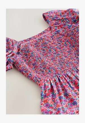 Sukienka w kwiatowy wzór z marszczoną górą, bufkami na rękawach i falbaną u dołu, w żywych odcieniach różu, fioletu i czerwieni.