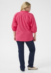 Blusa rosa con maniche a sbuffo, design testurizzato e scollo rotondo. Abbinata a jeans blu scuro e ballerine chiare.