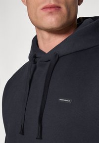 Navyblauer Hoodie mit Kordelzug, aus einem Baumwollmischgewebe gefertigt. Verfügt über ein kleines Markenetikett auf der Brust und eine weiche Textur.