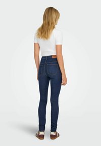 Granatowe, przylegające jeansy z wysokim stanem, z dwoma tylnymi kieszeniami i kontrastowymi detalami przeszyc. Połączone z białym obuwiem.