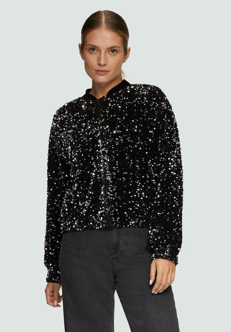Zwarte sequined blazer met een ronde halslijn en lange mouwen, met een gestructureerd, glanzend oppervlak, gecombineerd met donkerdenim jeans.