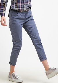 Modré bavlněné chinos kalhoty s uvolněným střihem, středním pasem, manžetami na nohavicích a bočními kapsami, sladěné se stříbrnými teniskami.